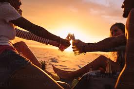 https://us.images.westend61.de/0001746381pw/friends-having-a-party-sitting-near-the-beach-at-sunset-smiling-friends-on-a-holiday-toasting-drinks-sitting-on-beach-with-sun-in-the-background-JLPSF18697.jpg